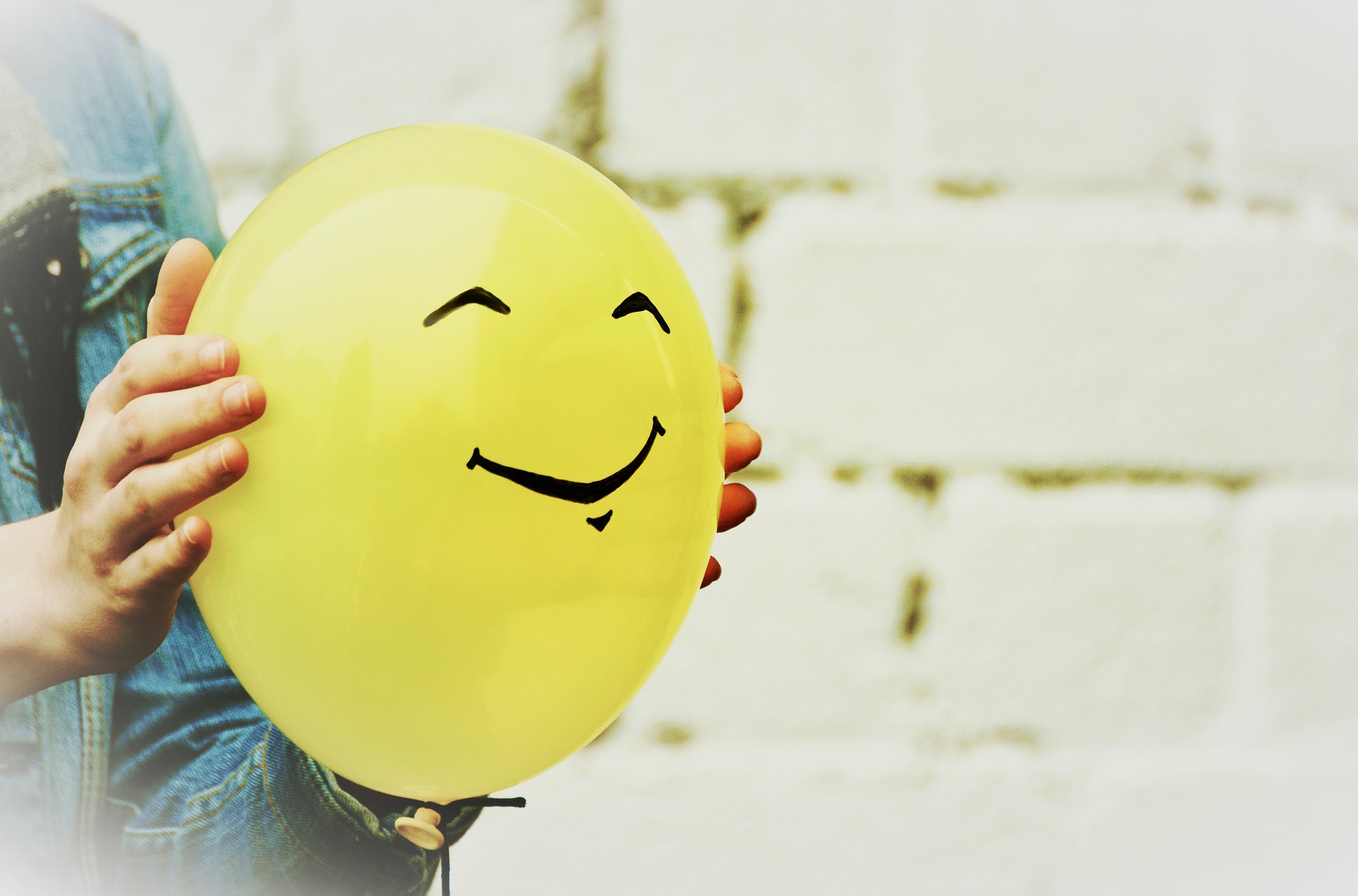 Hands holding yellow smiling balloon.