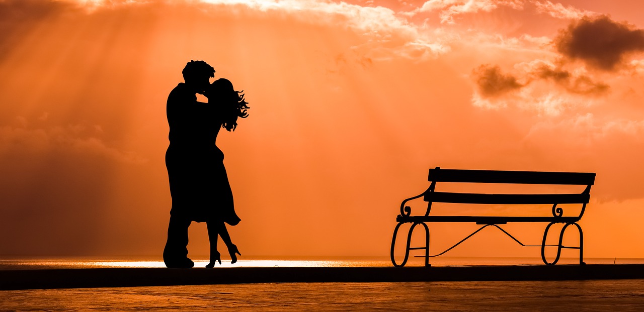Romance loving couple in orange sunset with bench